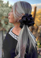 Person with silver hair tied back with a black scrunchie, standing outdoors.