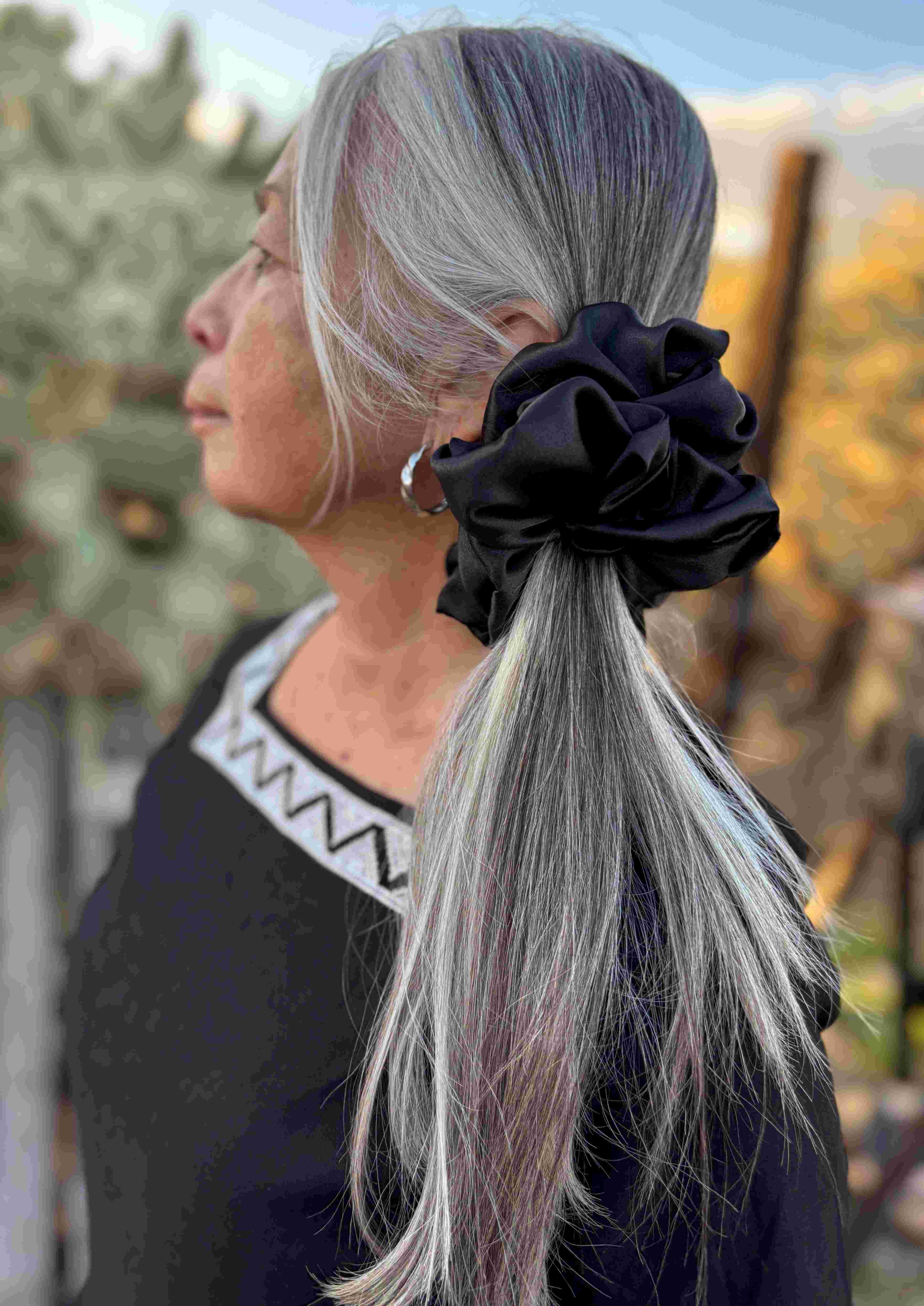 Person with silver hair tied back with a black scrunchie, standing outdoors.