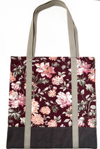 Tote bag with pink floral pattern on a dark red background, with brown bottom and tan bag straps
