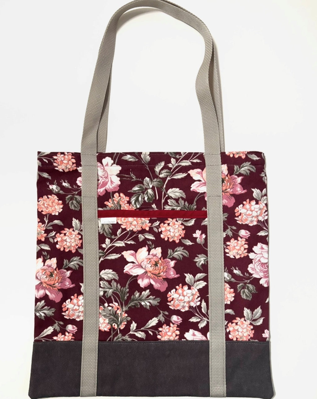 Tote bag with pink floral pattern on a dark red background, with brown bottom and tan bag straps