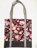 Tote bag with pink floral pattern on a dark red background, with brown bottom and tan bag straps