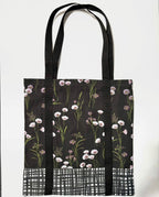 Tote bag with white floral pattern on a black background, with black and white line pattern bottom and black bag straps