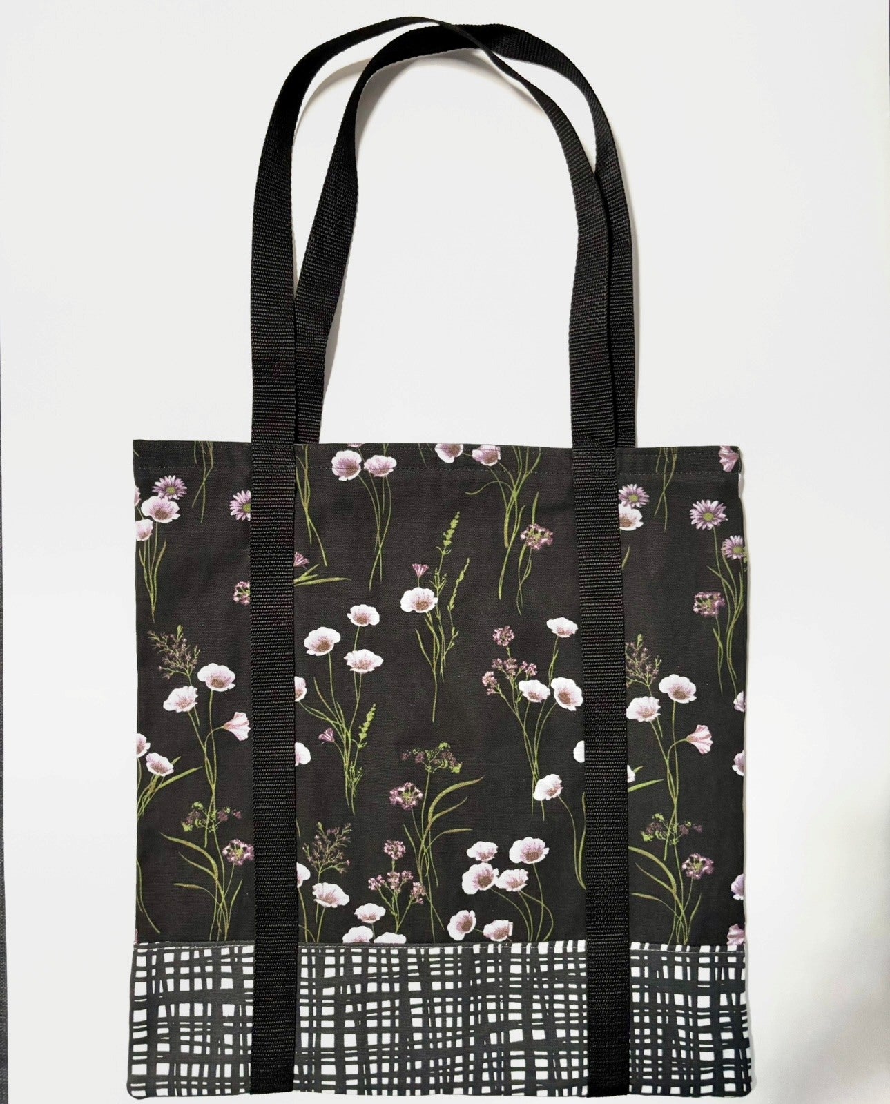 Tote bag with white floral pattern on a black background, with black and white line pattern bottom and black bag straps