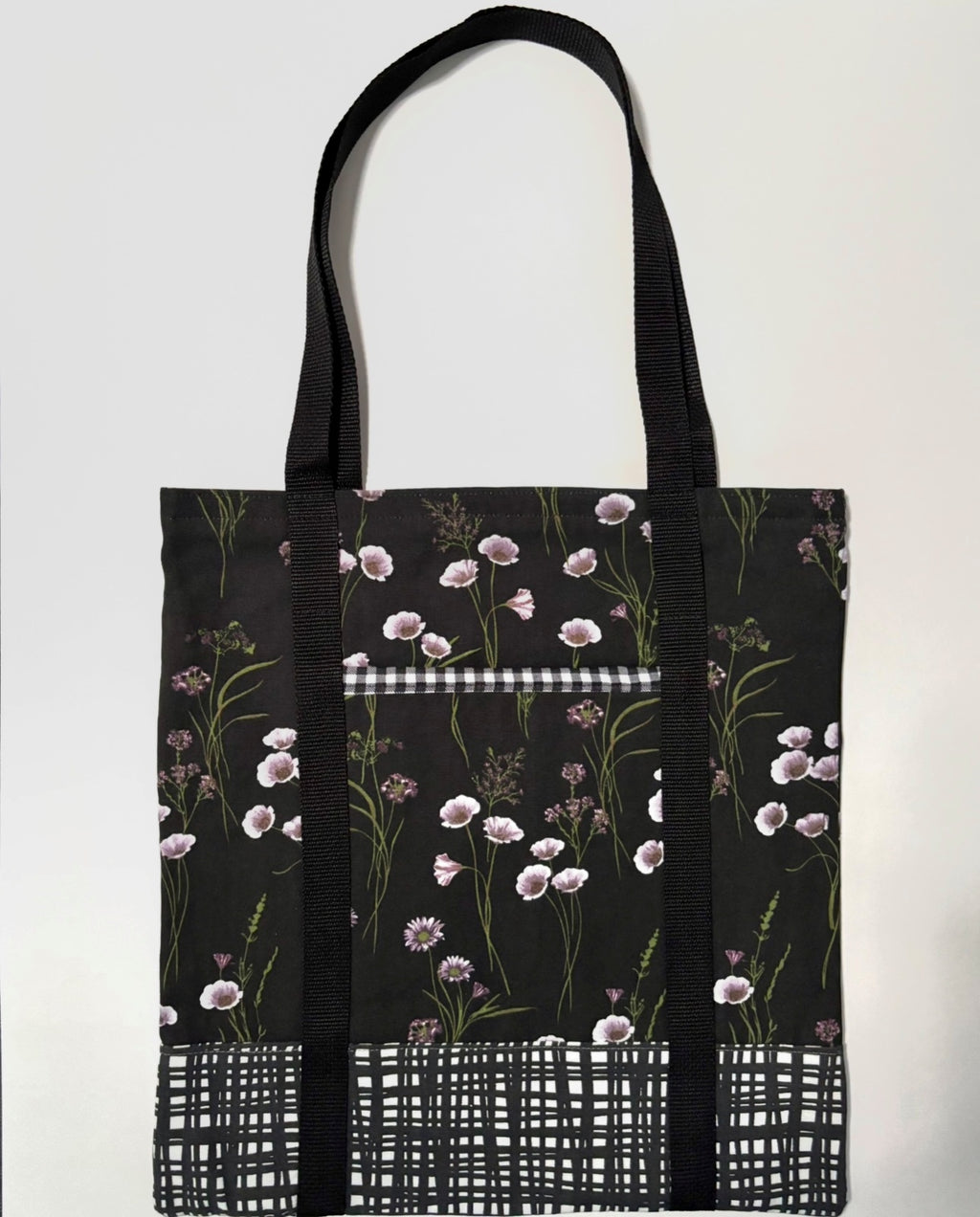 Tote bag with white floral pattern on a black background, with black and white line pattern bottom and black bag straps