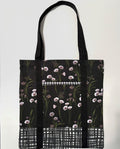 Tote bag with white floral pattern on a black background, with black and white line pattern bottom and black bag straps