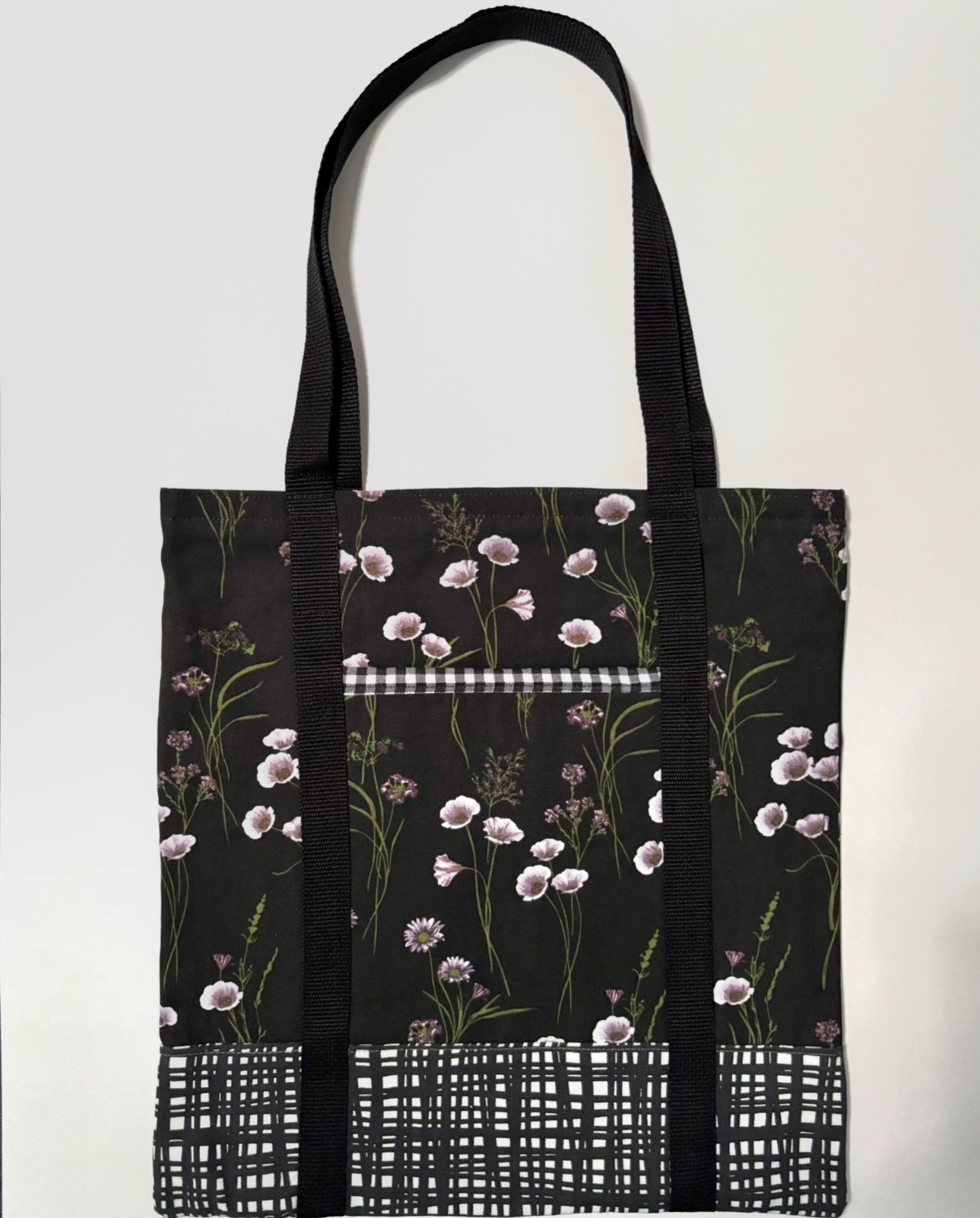 Tote bag with white floral pattern on a black background, with black and white line pattern bottom and black bag straps